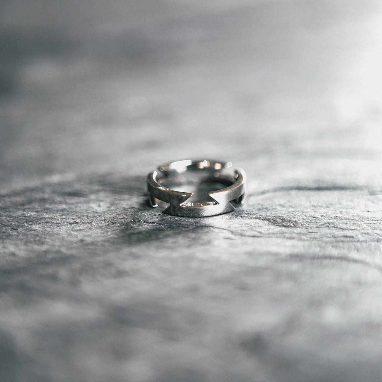 Single silver-colored titanium ring with zig-zag pattern, 6 mm thick. Image shows ring laying on a rough surface.