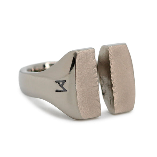 Single silver-colored titanium signet ring, 15x15 mm wide surface which has been cut through the middle. Image shows corner view of the ring