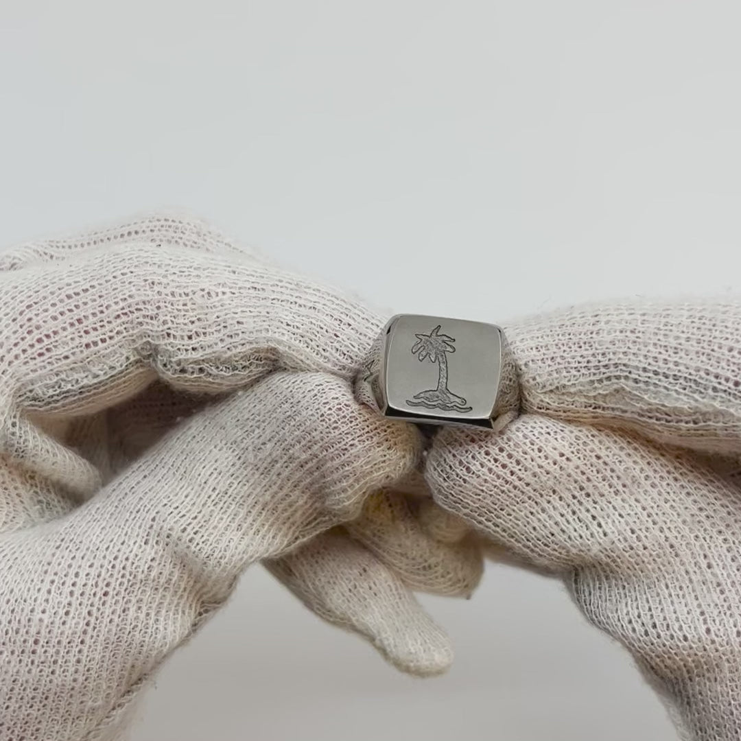 Showing single silver-colored titanium signet ring, 15x15 mm wide surface with an engraved palm tree from all angles.